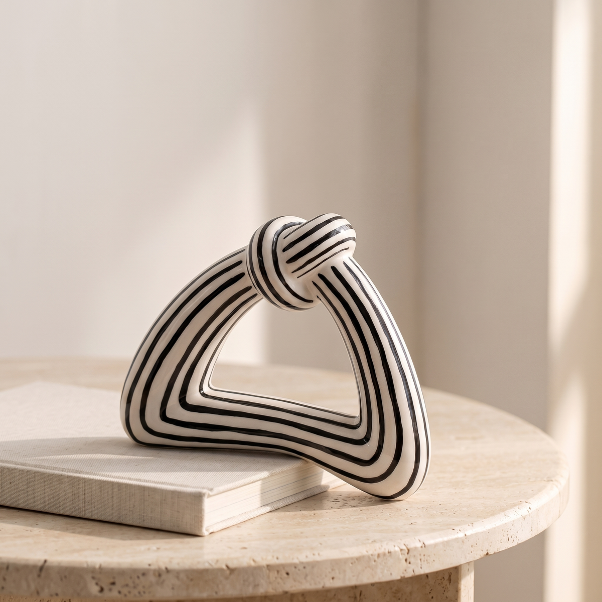 Black and white striped ceramic knot sculpture displayed in a warm modern interior