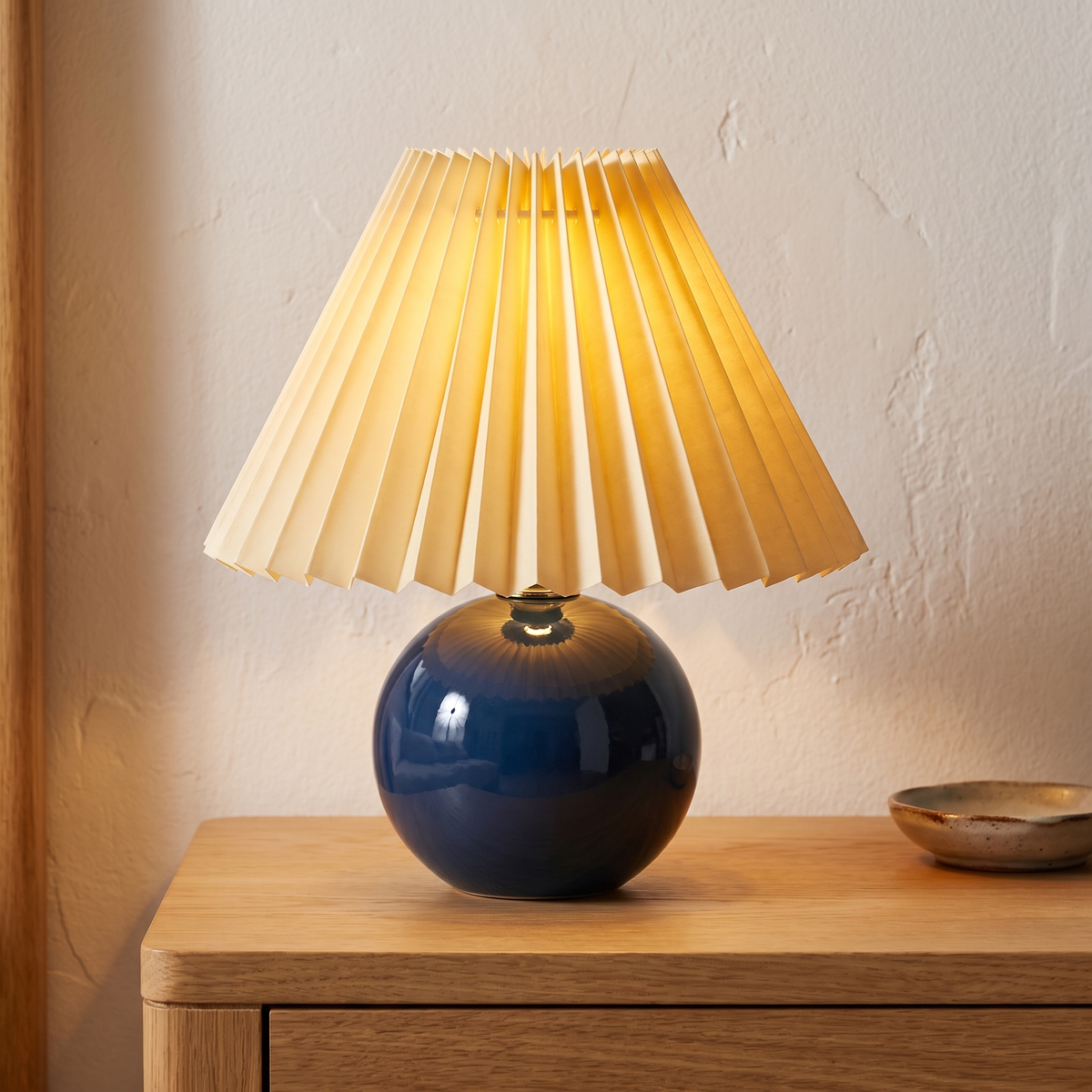 Navy ceramic lamp with pleated shade displayed in a warm modern interior